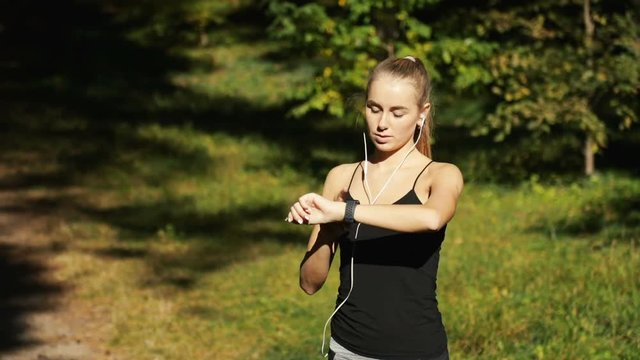 Attractive girl looking at watch to track the time while doing exercise, outdoor shot on great fall day, concept of sensible approach in any kind of sports activities