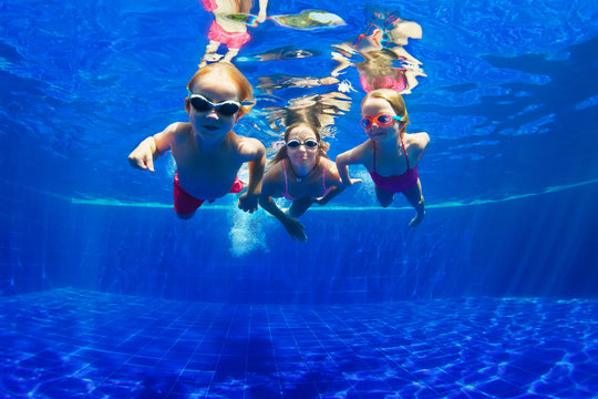 Happy family - mother, baby son, daughter in goggles swim, dive in pool with fun - jump deep down underwater. Healthy lifestyle, people water sport activity, swimming lessons on holidays with kids