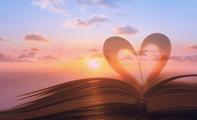 Heart shape from book against peaceful sunset. Reading, religion, love concept. Double exposure. 