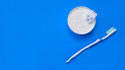 The figure of the tooth is smiling in an open jar of tooth powder. The view from the top. Flat lay.