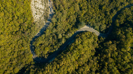 Aerial view of curvy rural road in mountains in autumn season. Cars driving below on the road.