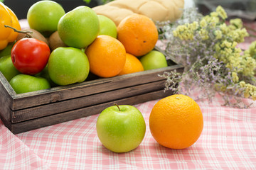 Orange and apple in a wooden crate. Fresh fruit on a wooden table with a cloth. Eating fruit helps to lose weight. fruits and vegetables in wooden box on table in kitchen.