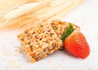 Homemade organic granola cereal bars with nuts and dried fruit on white background with oats and raw wheat and strawberry
