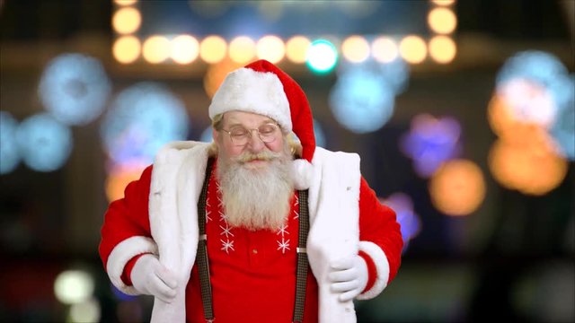 Happy Santa Claus in eyeglasses is dancing. Portrait of smiling elderly man in costume of Santa Claus on blurred background. Christmas theme.