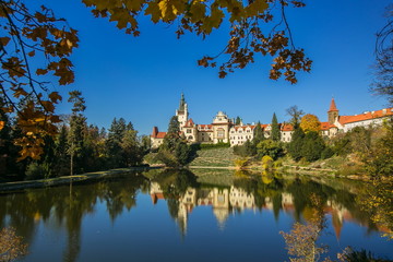 Fototapeta na wymiar Beautiful fall scenery of famous Pruhonice castle, Czech Republic, Europe, standing on hill, sunny day, blue sky, reflection in lake, yellow maple leaves in foreground, colorful trees