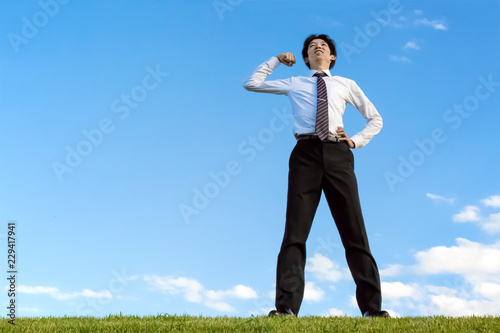 青空をバックにガッツポーズで見上げるyシャツ姿の若い男性1人 ヤル気 挑戦 成功 努力 目標イメージ Wall Mural Chikala