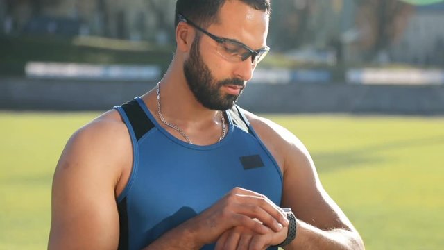 Attractive, intelligent man looking at watch to track the time while doing exercise, outdoor shot on great fall day, concept of sensible approach in any kind of sports activities