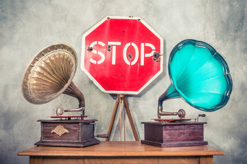 Antique gramophone phonograph turntables with brass and turquoise horns on wooden table and retro aged STOP road sign front concrete wall background. Vintage old style filtered conceptual photo