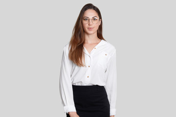 Photo of attractive elegant woman in business style, wears transparent glasses, white blouse and black skirt, isolated over white background. Stylish female businesswoman ready to work in office