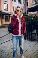 A girl in sneakers with shoes in her hands, talking on the phone in the street. The end of the working day.