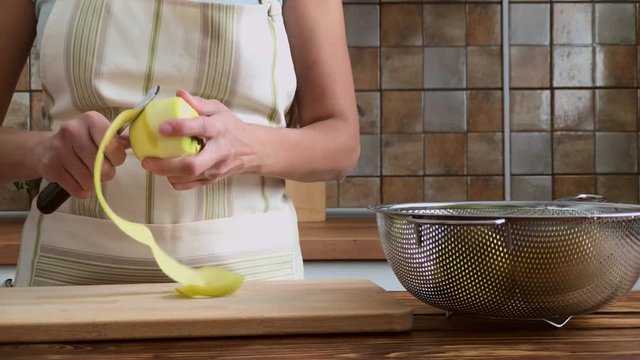 Woman is peeling green aples on the kitchen, slow motion