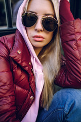 Stylish hipster girl in the retro jeans suit posing in front of the old brick wall. Trendy young woman with bag standing next to old building. Street fashion concept, wearing glasses