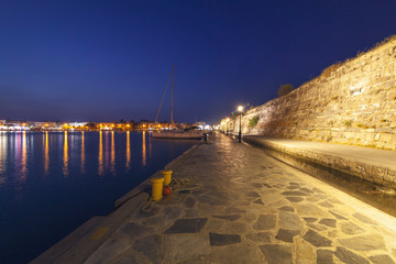 The wall of the old castle fortress in the city of Kos, Greece, night city landscape, view of the port with yachts and boats