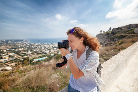 Beautiful young woman with a camera in hand, traveler and bloggen on the background of a beautiful landscape with mountains and sea