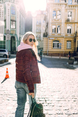 Obraz premium Street fashion concept - portrait of a beautiful girl sitting outside, blue jeans, sunglasses, hard lights, red jacket, autumn weather