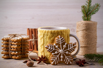 Knitted yellow cup with hot winter drink, cookies, cinnamon, decorations. Cozy