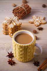 Knitted yellow cup with hot winter drink, cookies, cinnamon, decorations. Cozy