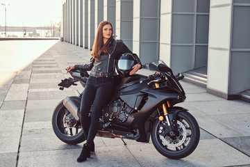 Naklejka na ściany i meble A beautiful biker girl leaning on her superbike outside a building.