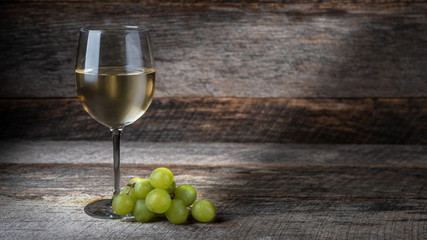 glass of white wine and grapes on wooden background