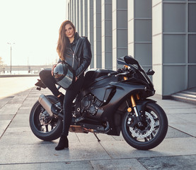 Fototapeta na wymiar A beautiful biker girl leaning on her superbike outside a building.