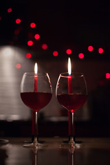 Romantic dinner: two glasses of wine and candels are in the dark with new year lights at the background