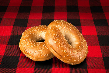 Fresh sesame seed bagel bread, isolated on a tartan red and black tablecloth in background.