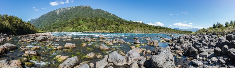 Fototapeta na wymiar Panoramic landscape of the Petrohue River full of big stones with a forested little mountain chain