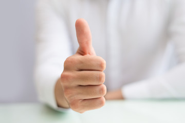 Close-up of male hand showing thumb-up expressing positive estimation. Unrecognizable man sitting at table and gesturing. Approval concept 