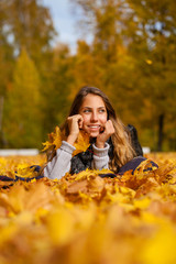 Fototapeta na wymiar Happy little girl lies down on leaves at the park on beautiful autumn day