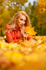 Naklejka na ściany i meble Beautiful blond hair woman lies down on leaves at the park on beautiful autumn