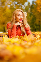 Beautiful blond hair woman lies down on leaves at the park on beautiful autumn