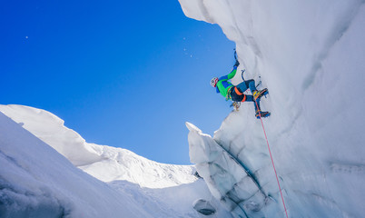 Epic shot of an ice climber climbing on a wall of ice. Mountaineer, climber or alpinist on an...