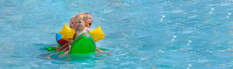 Drei Kleinkinder mit Riesenspaß auf einem Schwimmkrokodil im Schwimmbad