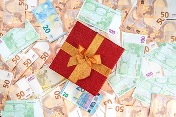 Background from banknotes of different value. A precious red gift. Top view.