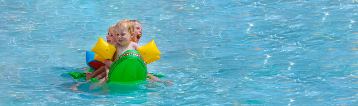 Drei Kleinkinder mit Riesenspa&szlig; auf einem Schwimmkrokodil im Schwimmbad