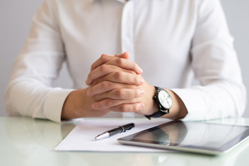 Close-up of male executive sitting at table with clasped hands. Caucasian hr manager working at table with papers and digital tablet. Employment concept