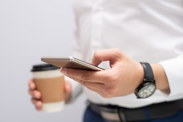 Close-up of male hand texting message on mobile phone. Caucasian businessman with coffee using smartphone. Mobile communication concept