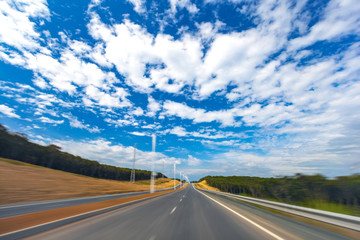 Asphalt road, highway, fenced off by chippers in dense forest with the effect of movement, under a beautiful blue sky with cumulus white clouds. Island Russian, Vladivostok, Primorsky region, Russia.