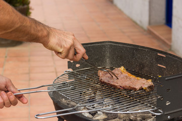 Man cooking steak on barbecue grill with big fork. Charcoal and fire flames to cook raw meat....