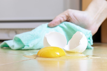 Fototapeta na wymiar Female hand removes broken egg with a tissue from kitchen floor