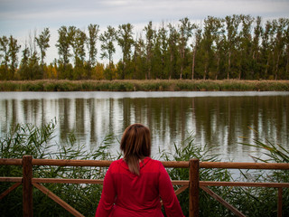 A young woman in a viewpoint with a wooden railing contemplating a river in autumn