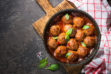 Meatballs in tomato sauce in a frying pan on dark stone table. 