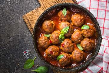 Meatballs in tomato sauce in a frying pan on dark stone table. 