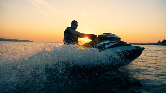 A man is riding a jet-ski along the coastline during sunset