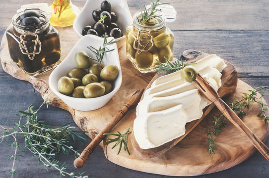aged brie cheese on a White dish with olives and Provence herbs wooden table
