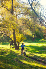 The girl rides a bike in the autumn park.