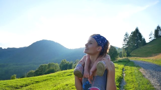 Young woman shows her daughter mountains. Mom and carries a daughter on her shoulders along a mountain serpentine.