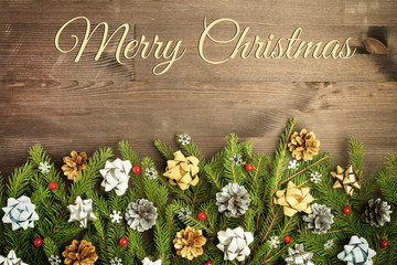 On a dark wooden background the inscription Merry Christmas. Below is a composition of fir branches, cones, bows and red ornamental berries.