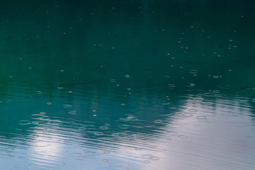 The turquoise surface of a lake with raindrops falling