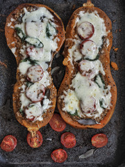 Baked halves of pumpkin stuffed with crushed meat, tomatoes and cheese. Seasonal meal. Overhead shot.